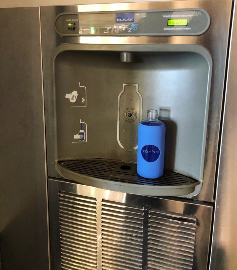PureFree Amico Deep Blue glass water bottle being refilled at water station